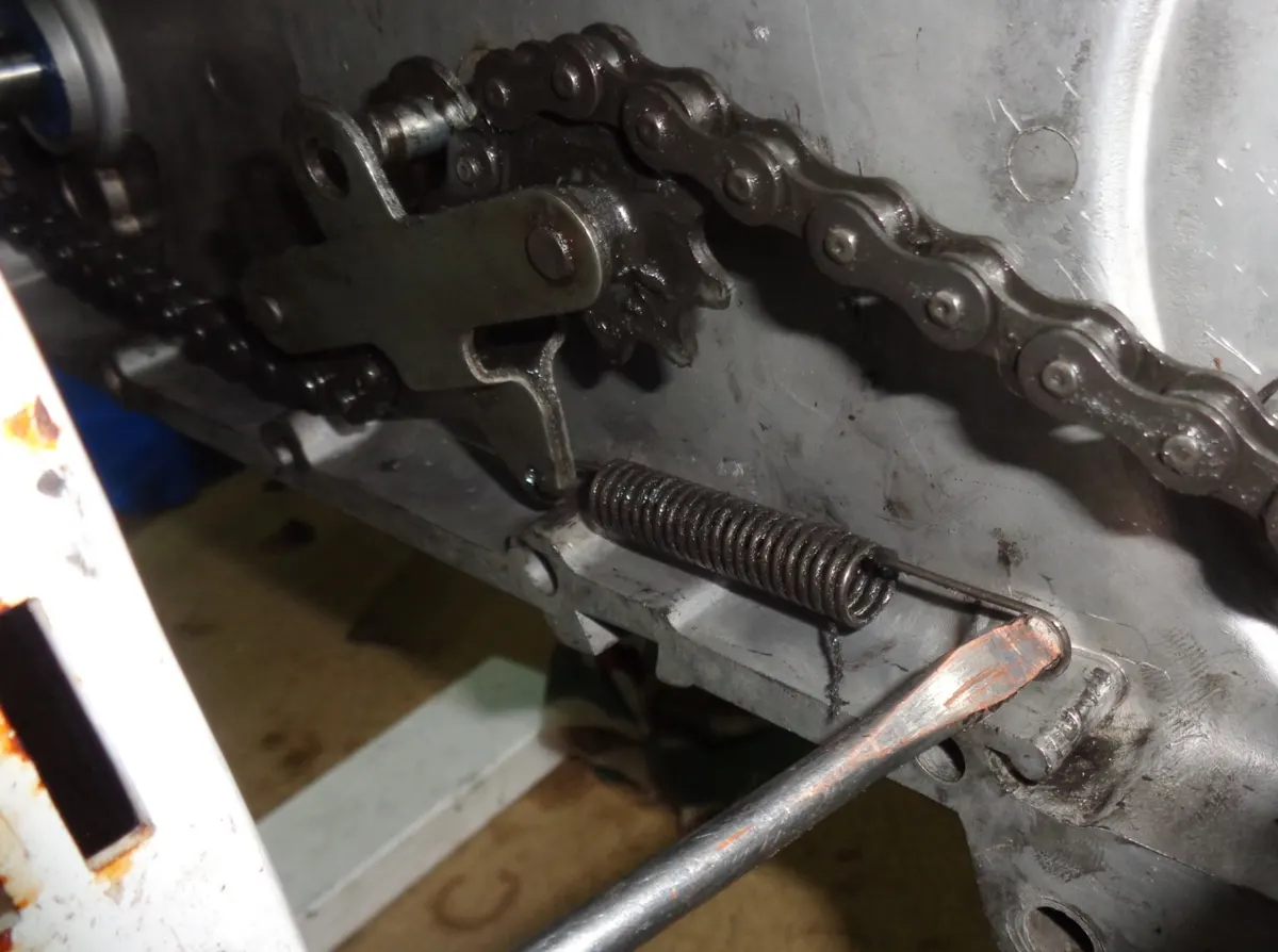 Tensado del muelle del tensor de cadena de vespino con un destornillador para anclarlo al carter.