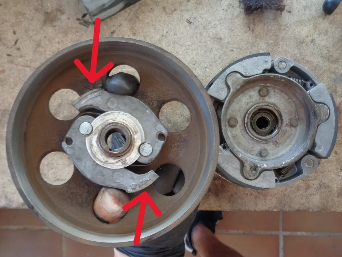 Ilustración de como montar la campana de embrague de vespino, comprimiendo las mordazas de arranque con los dedos a través de los huecos de la campana, con dos fleclas que indican la dirección de la compresión de las mordazas