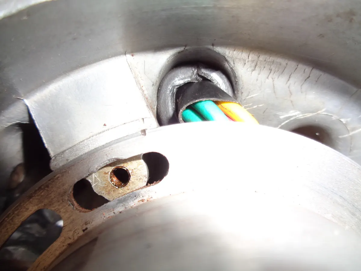 Detalle del pasacables por el que atraviesan los cables del estator de un vespino a través del carter