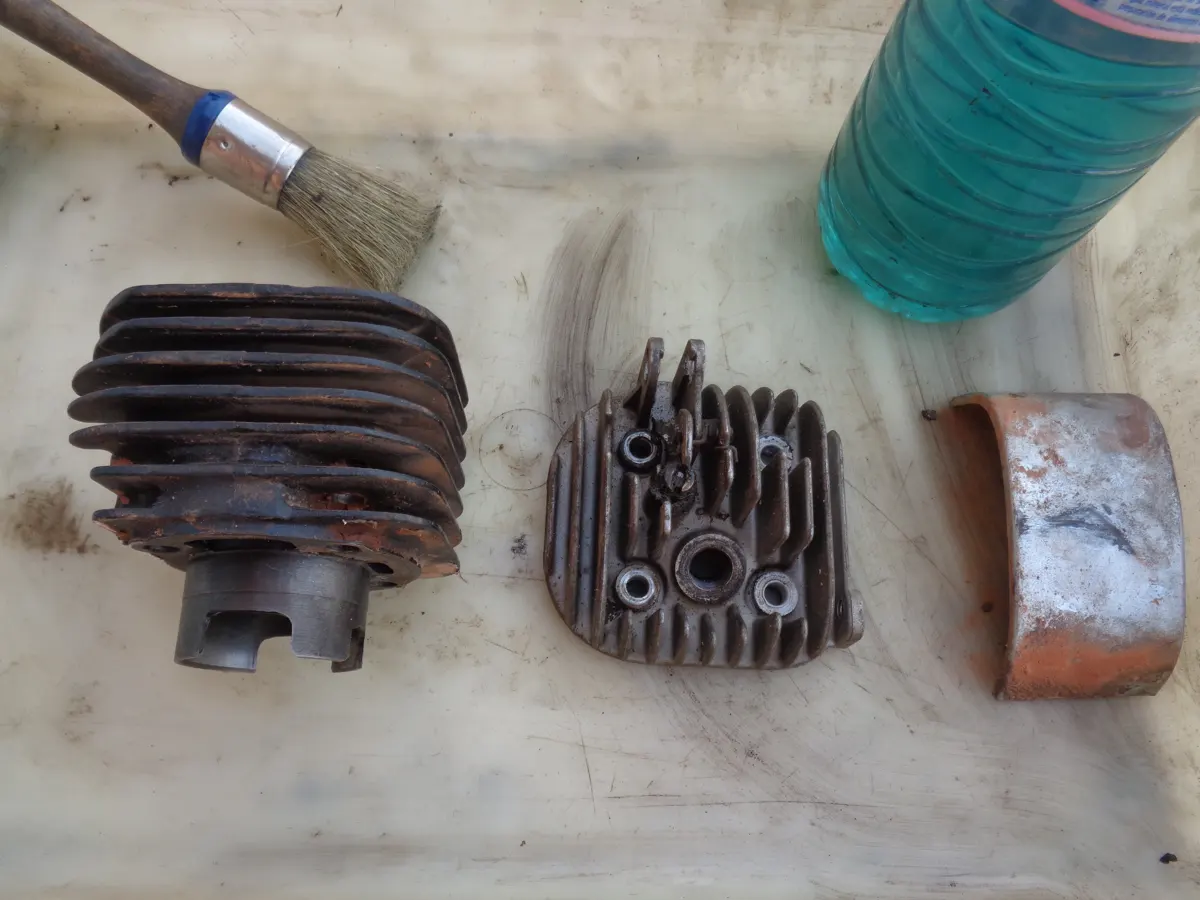 bandeja con una brocha y un bote de gasolina para limpiar un cilindro una culata y un deflector de vespino que se muestran