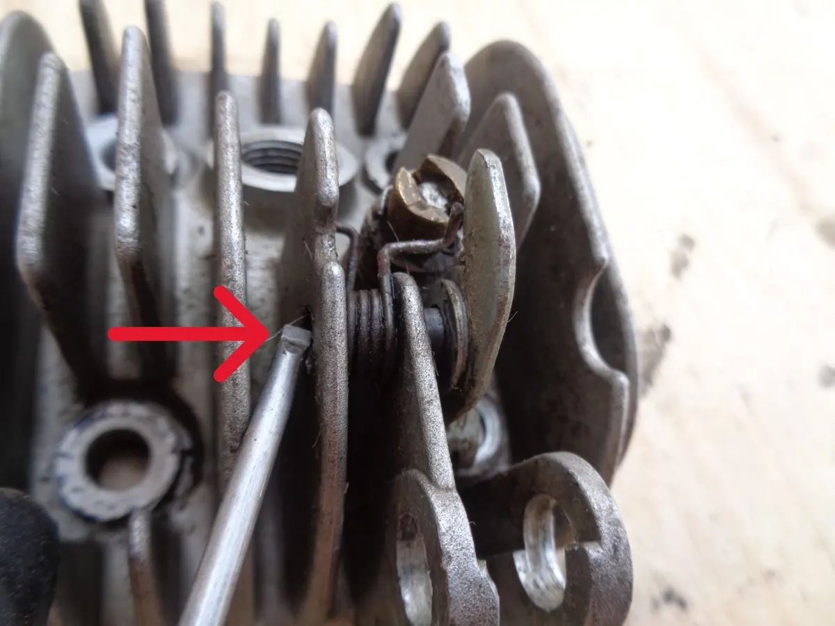 Ilustración con una flecha explicativa de la dirección para la extracción del pasador de la palanca del descompresor de la culata de un vespino