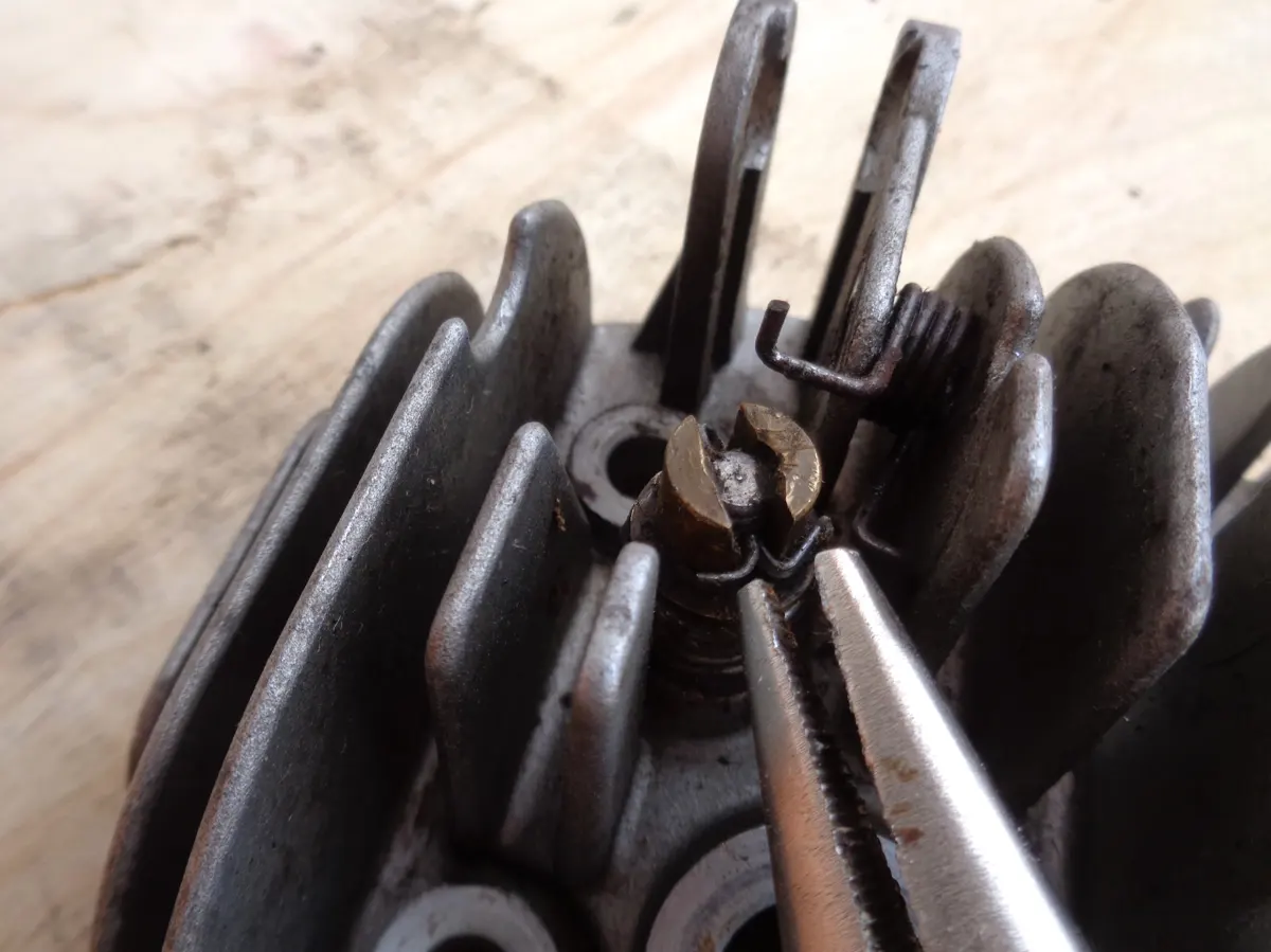 detalle del pasador de la válvula del descompresor de un vespino con un alicate de punta fina para retirarla