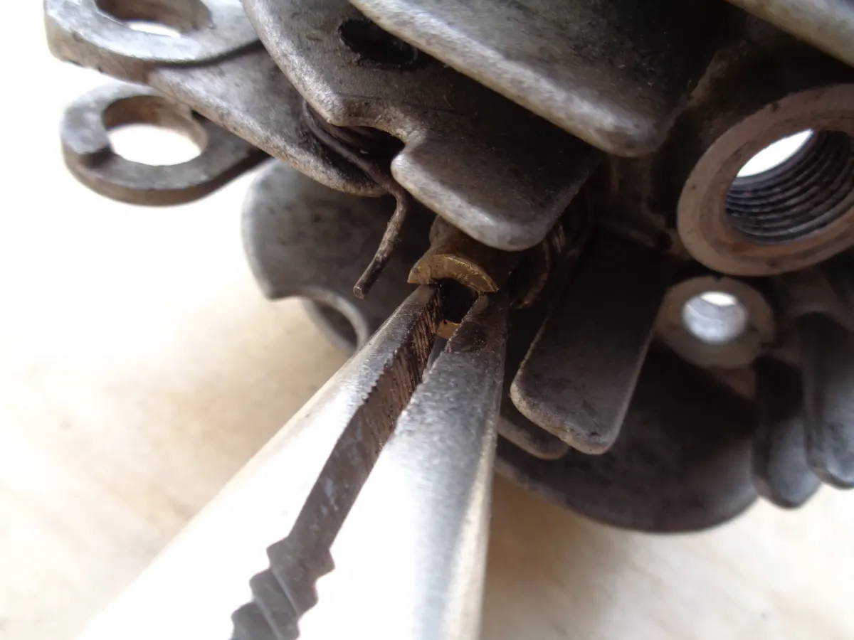 Alicate mordiendo el terminal de sujección del muelle del descompresor de la culata de un vespino en el proceso de desmontaje de la misma.