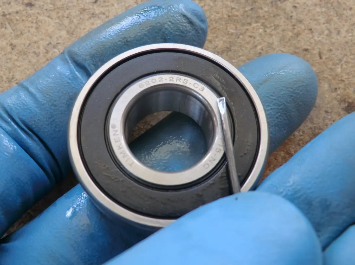 Rodamiento de cigüeñal de Vespino sellado al que se le está retirando con un destornillador, el sello para que se engrase al funcionar