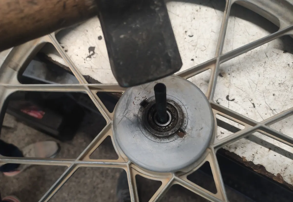 Detalle del proceso de extracción de rodamietnos de una rueda delantera de un Vespino, en la que un puntero empuja el rodamiento de la rueda y un martillo lo golpea para extraerlo
