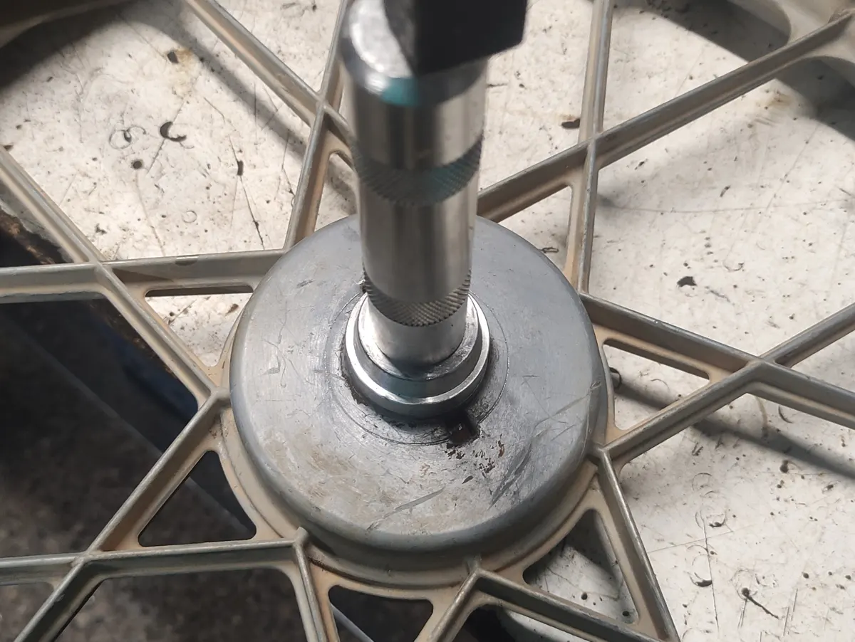 Detalle de la colocación de un rodamiento en la rueda delantera de un vespino con el útil para montar rodamientos siendo golpeado por un martillo