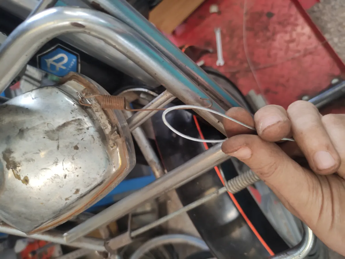 Detalle del proceso de montaje del faro de un vespino en el manillar, mostrando el cable que tirará del muelle
