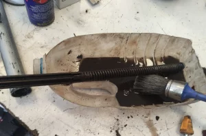Limpieza con brocha y gasolina de los muelles de suspensión de un vespino sobre una mitad de botella para recoger la mugre que cae