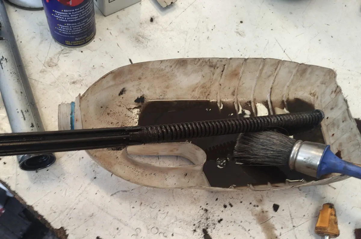 Limpieza con brocha y gasolina de los muelles de suspensión de un vespino sobre una mitad de botella para recoger la mugre que cae