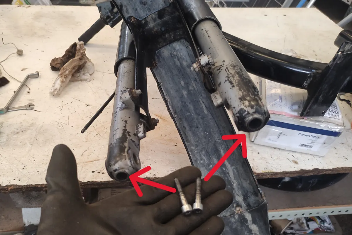 Vista inferior de las botellas de suspensión de un vespino indicando los tornillos que las atraviesan anclando la suspensión